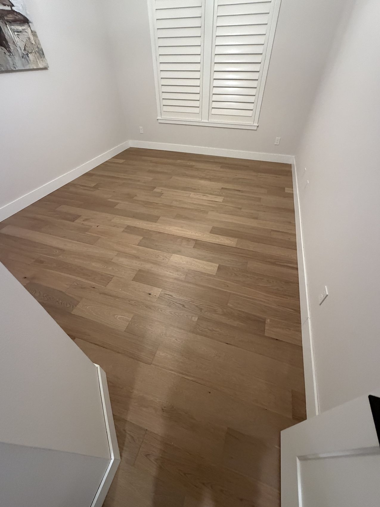 Finished light engineered oak hardwood floor in an upstairs bedroom with white baseboard