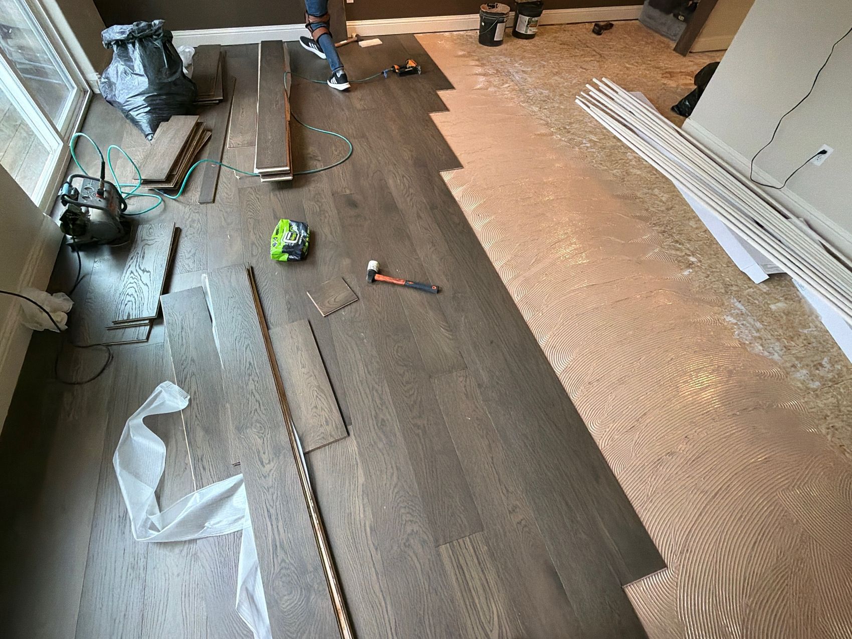 Dark engineered oak hardwood being glued down over a troweled subfloor in a Portland-area living room